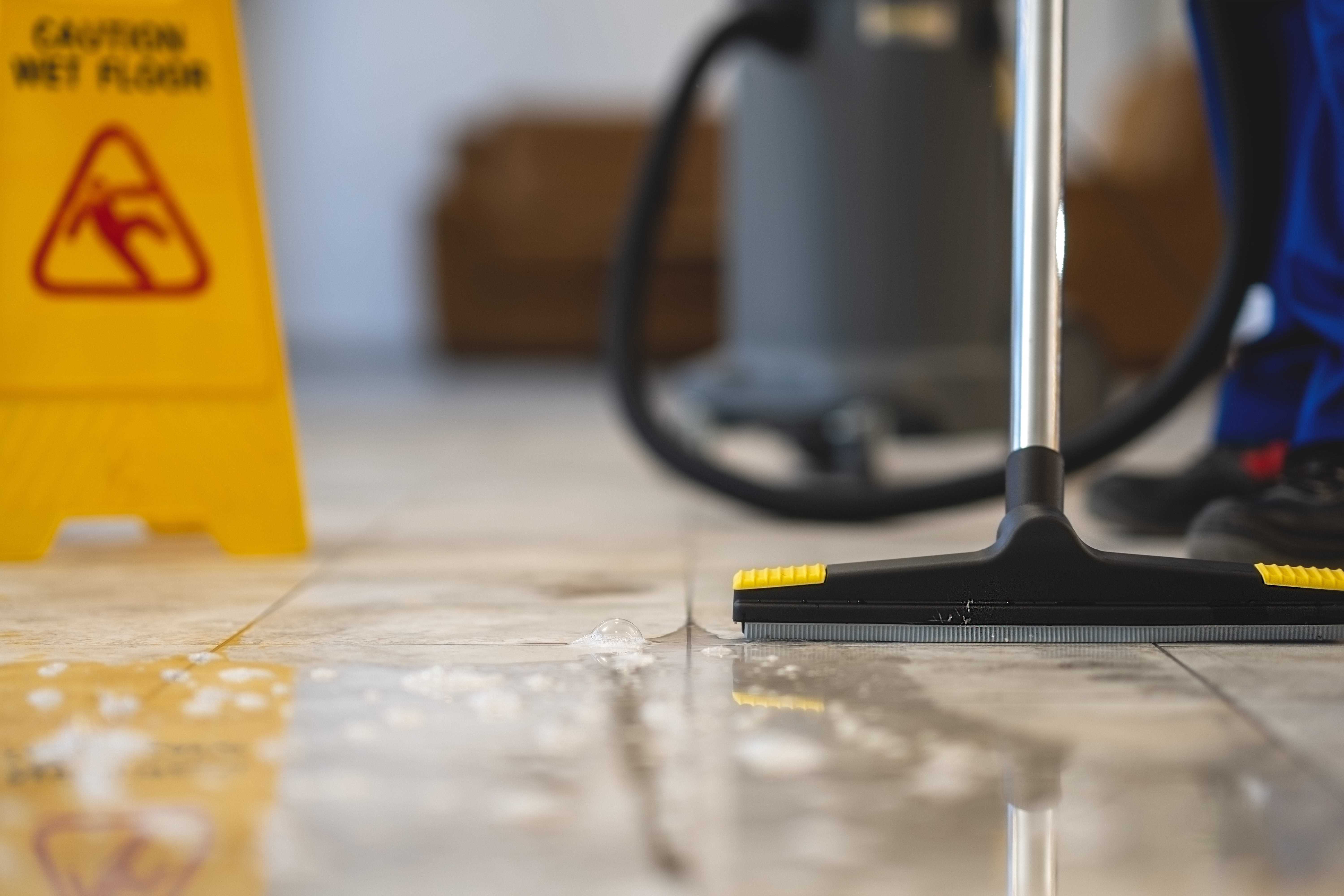 Wet floor being cleaned with squeegee next to yellow wet floor caution sign